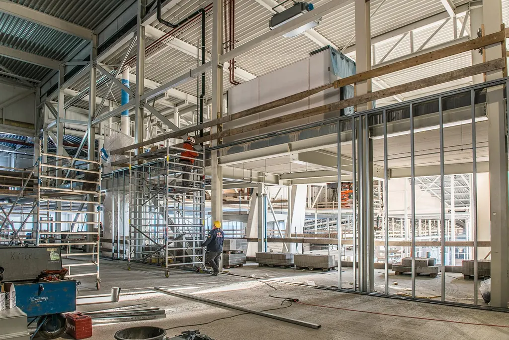 Bouwplaats met metal stud frames voor nieuwe wanden, steigers en een monteur met helm
