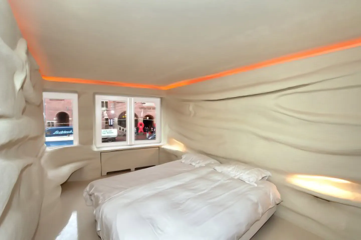 Hotelkamer met wanden in stuc die geplooid zijn als stof, met indirect oranje licht langs het plafond