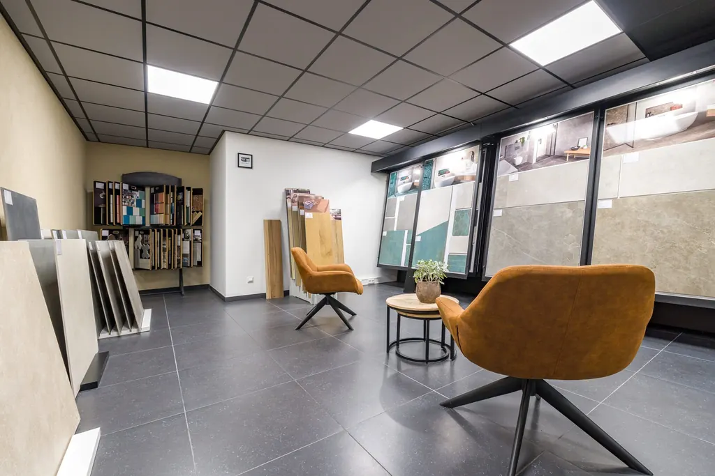 Showroom van SB Afbouw met grote tegels, stalenwand en twee oranje stoelen